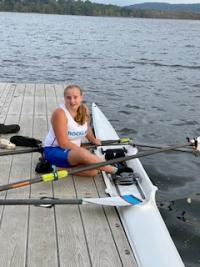 Teen athlete Leila sits on the dock next to her single scull (narrow shell for a single rower).